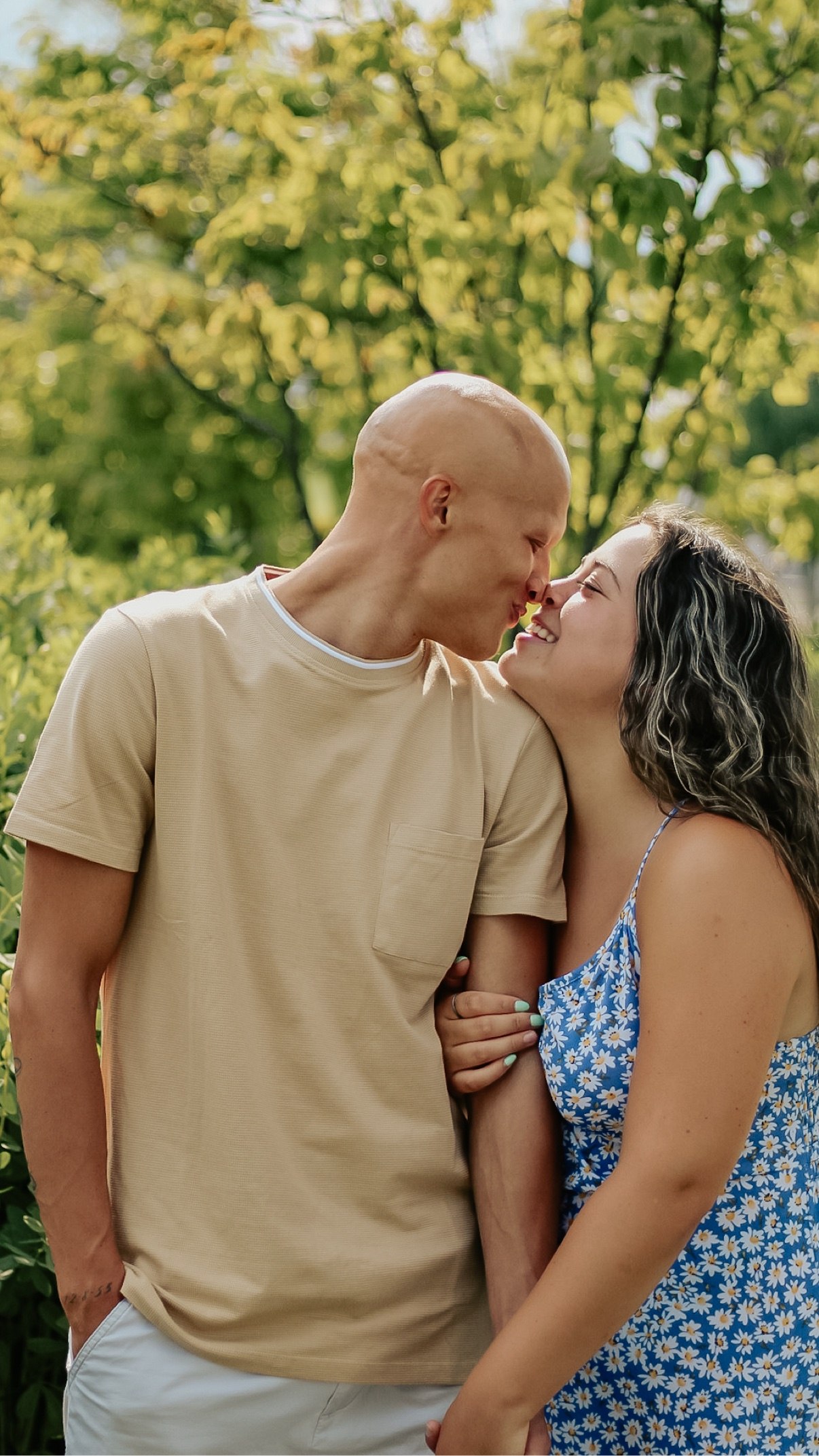 Couple nose to nose and smiling in front of green summer trees