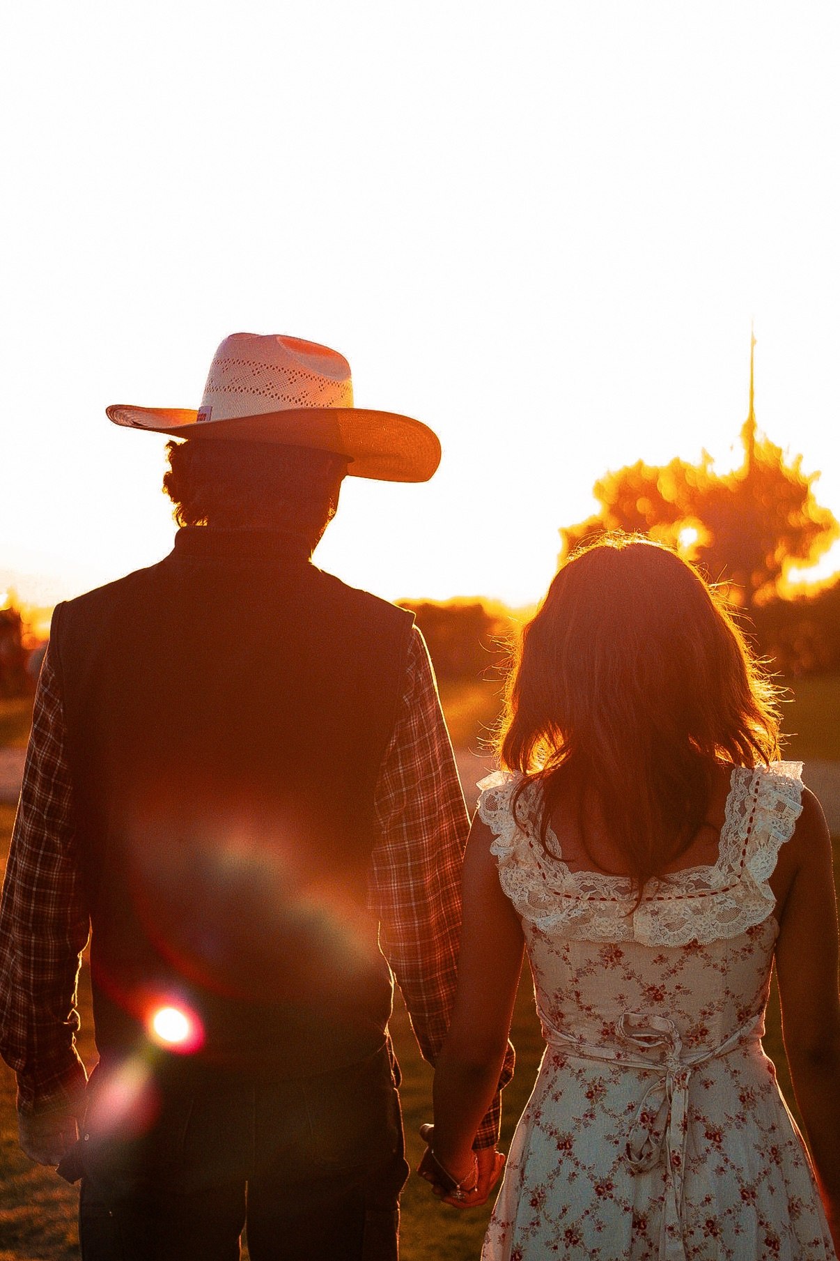 Couple seen from behind holding hands and walking toward the sunset, the man in a cowboy hat